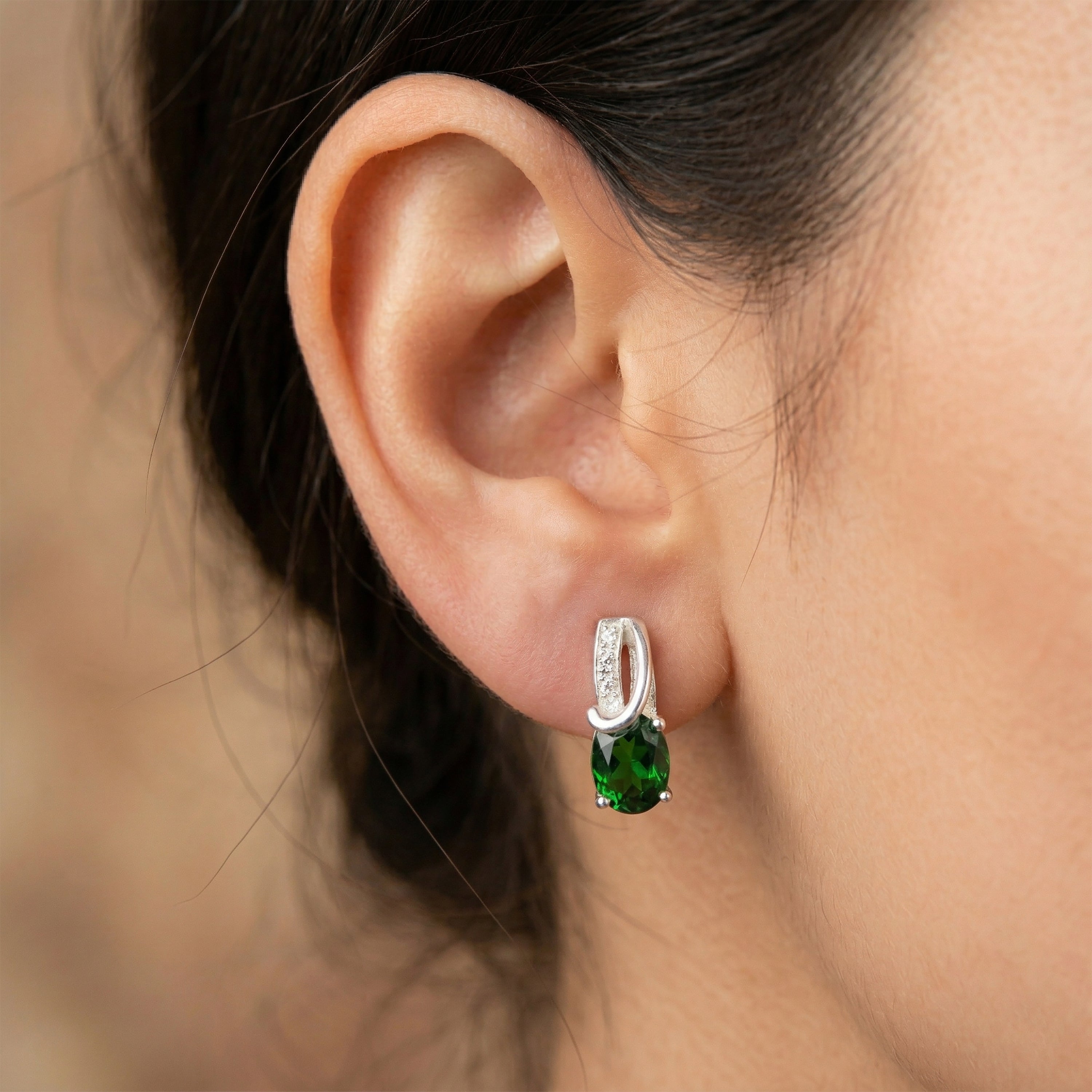 Close-up of a model wearing Faris Jewels oval emerald and white quartz drop earrings in 925 sterling silver